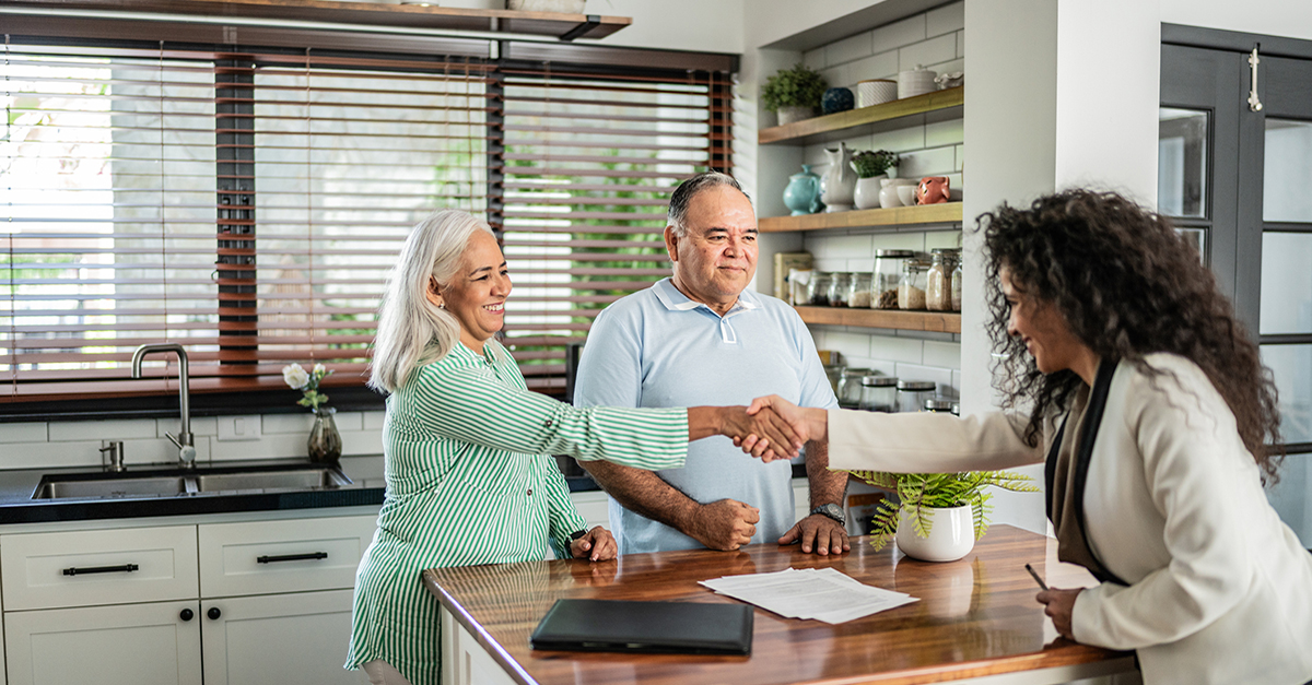 An agent shaking hands with her clients in their kitchen