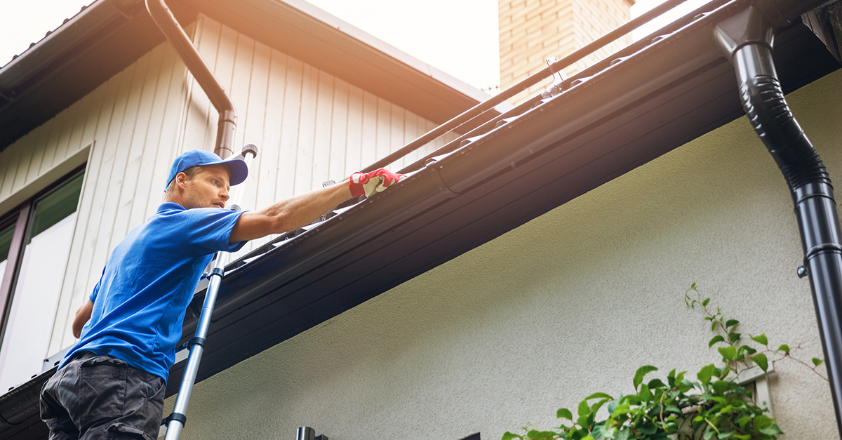 A man on a ladder cleaning out the gutters